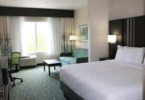 Habitación de hotel con una cama grande, un escritorio, una silla, un sofá y una ventana con cortinas.