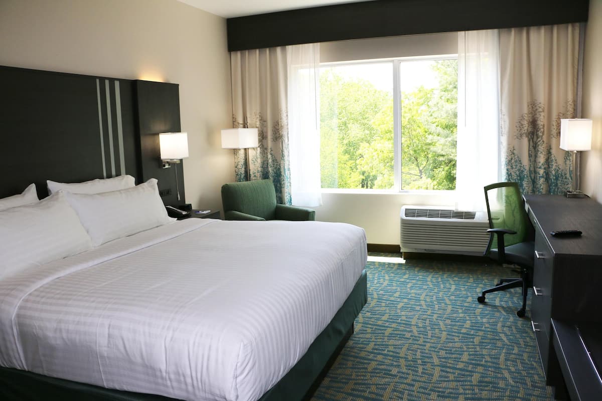 A hotel room with a large bed, two chairs, a desk, and a window with curtains.