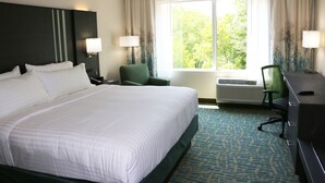 A hotel room with a large bed, two chairs, a desk, and a window with curtains.