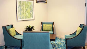 A room with two teal upholstered chairs, a small table, and a framed abstract painting on the wall.