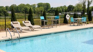 A swimming pool with lounge chairs and tables, surrounded by a fence and greenery.