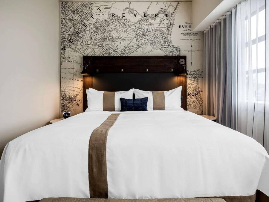 A hotel room with a large bed, a dark headboard, and a map on the wall.