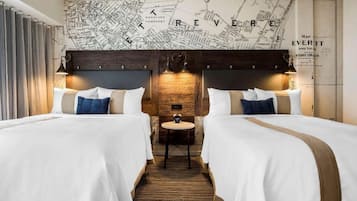 Quarto de hotel com duas camas, uma cabeceira de madeira, um mapa na parede e uma pequena mesa com um relógio.