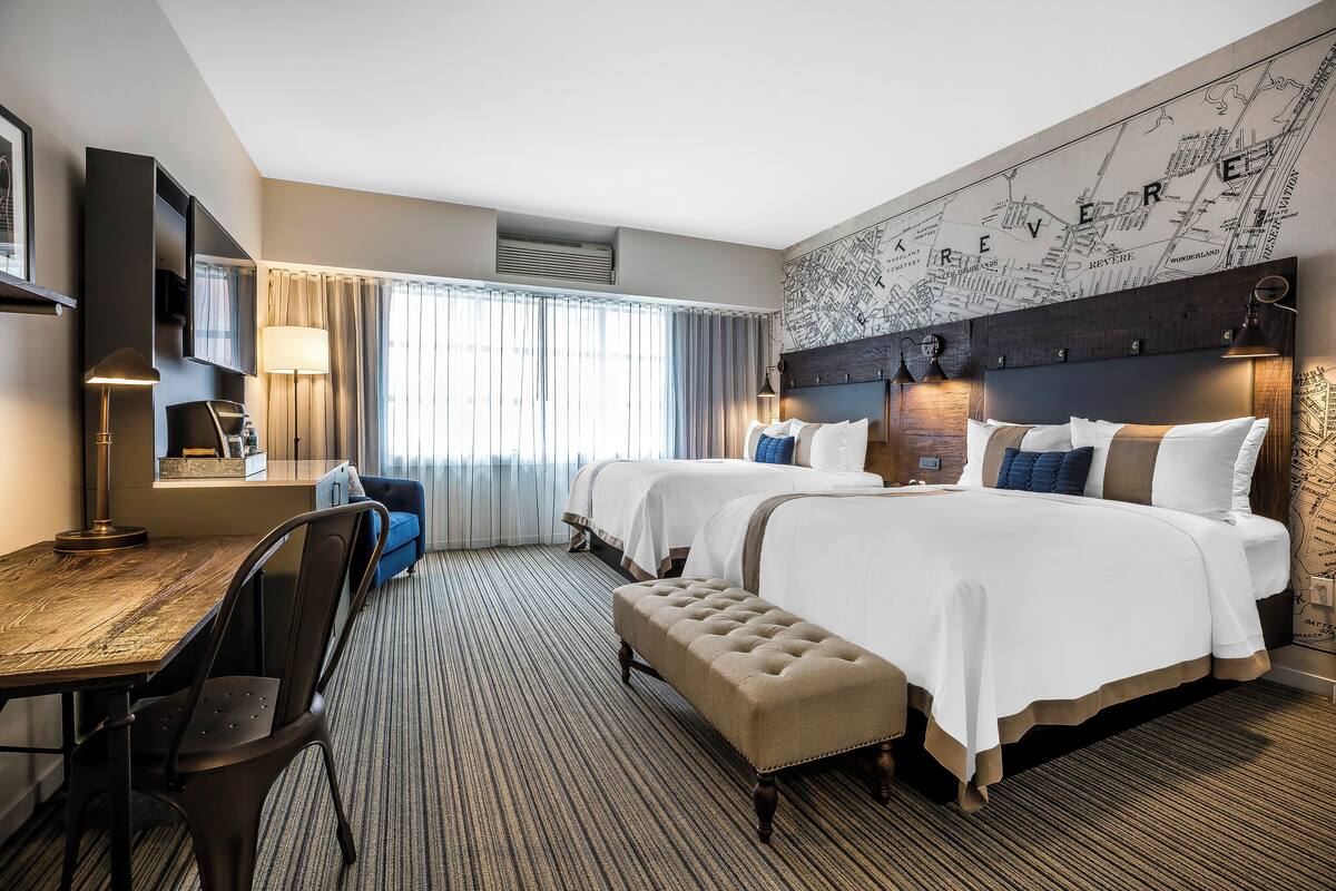 Une chambre d’hôtel avec deux lits, un bureau, une chaise et une grande fenêtre avec des rideaux.