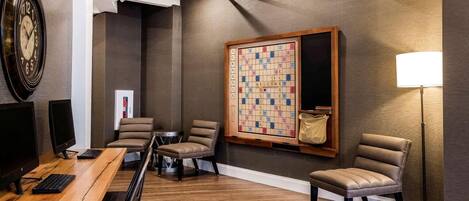 Una habitación moderna con un escritorio de madera, dos sillones de cuero, un tablero de ajedrez grande y una lámpara de pie.