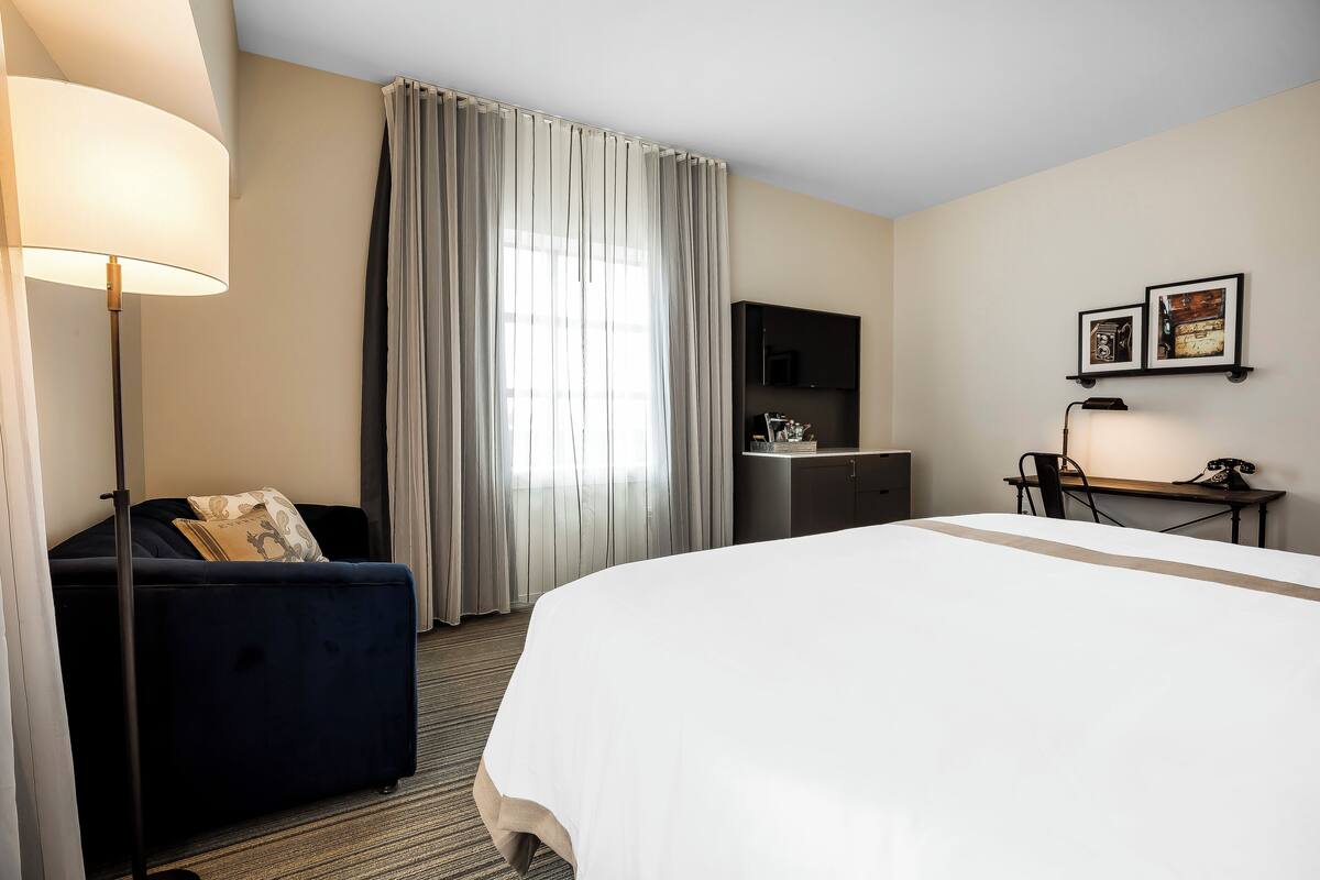 Une chambre d’hôtel avec un grand lit, un bureau, une chaise, un canapé, une télévision et une lampe.