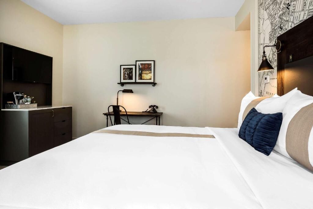 Habitación de hotel con una cama, un escritorio, una silla, un televisor y cuadros en la pared.