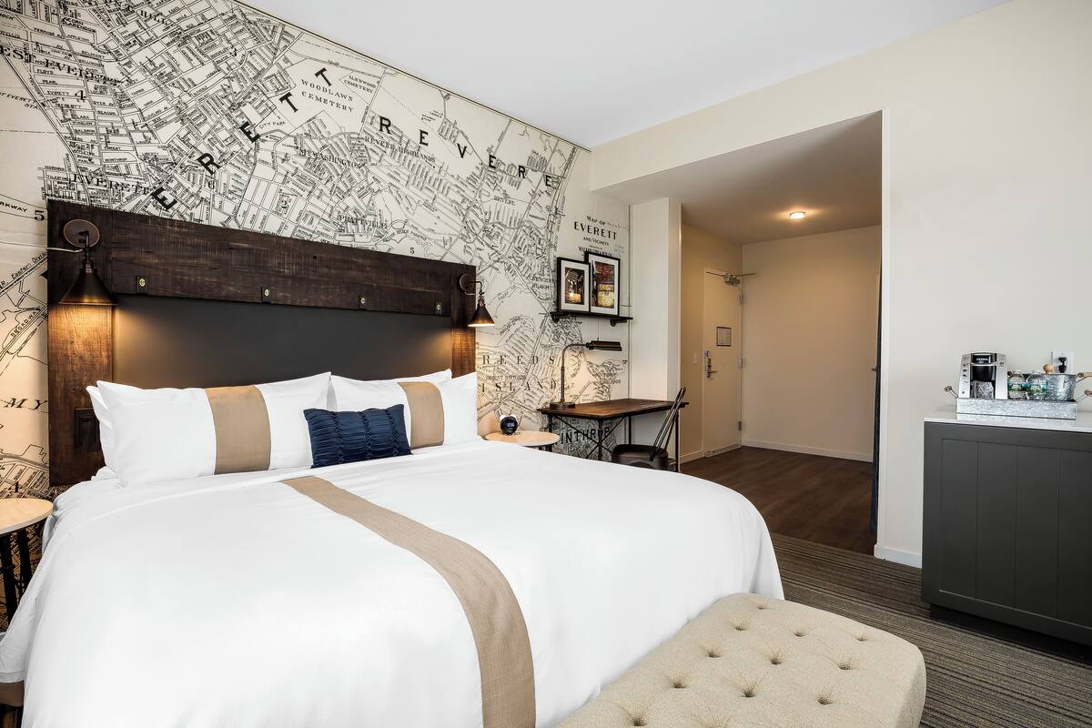 Une chambre d’hôtel avec un grand lit, un mur décoré d’une carte, un petit bureau et une kitchenette.