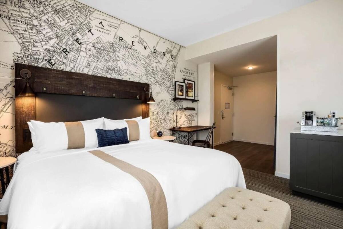 Une chambre d’hôtel avec un grand lit, une carte géographique peinte sur le mur, une petite table et un coin cuisine.