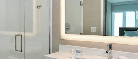 A modern bathroom with a glass shower enclosure, a large mirror, and two sinks.