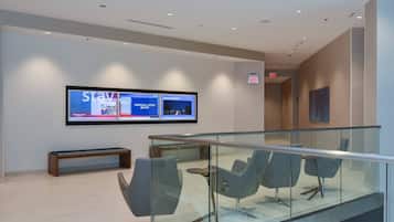 A modern hotel lobby with a large digital display, comfortable seating, and a glass railing.