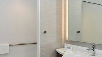 A modern bathroom with a walk-in shower, a large mirror, and a wooden vanity with a white sink.