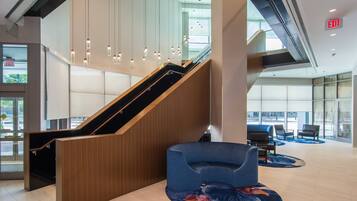 A modern lobby with a wooden staircase, seating area, and glass walls.