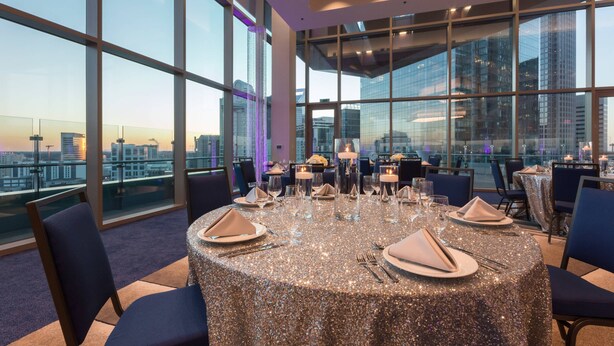 A dining area with a round table set for six, large windows offering a city view, and modern interior design. - SpringHill Suites Charlotte City Center (Charlotte)