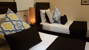 Habitación de hotel con dos camas, cada una con almohadas estampadas y una lámpara de noche.
