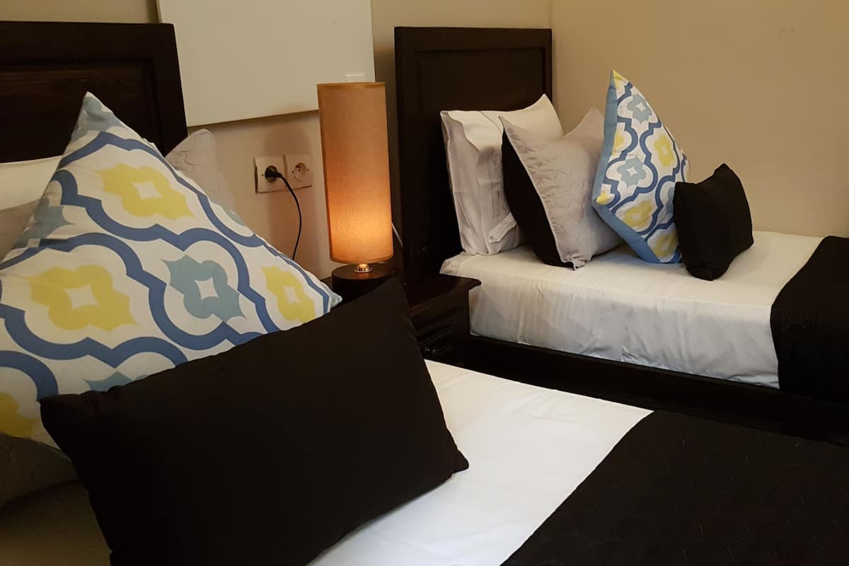 A hotel room with two beds, each with patterned pillows and a bedside lamp.