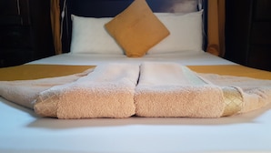 Una cama con un colchón blanco, dos toallas color beige y una sola almohada marrón.