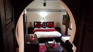 Una habitación de hotel con cama, mesitas de noche, lámpara, un cuadro y un objeto decorativo sobre la mesita.
