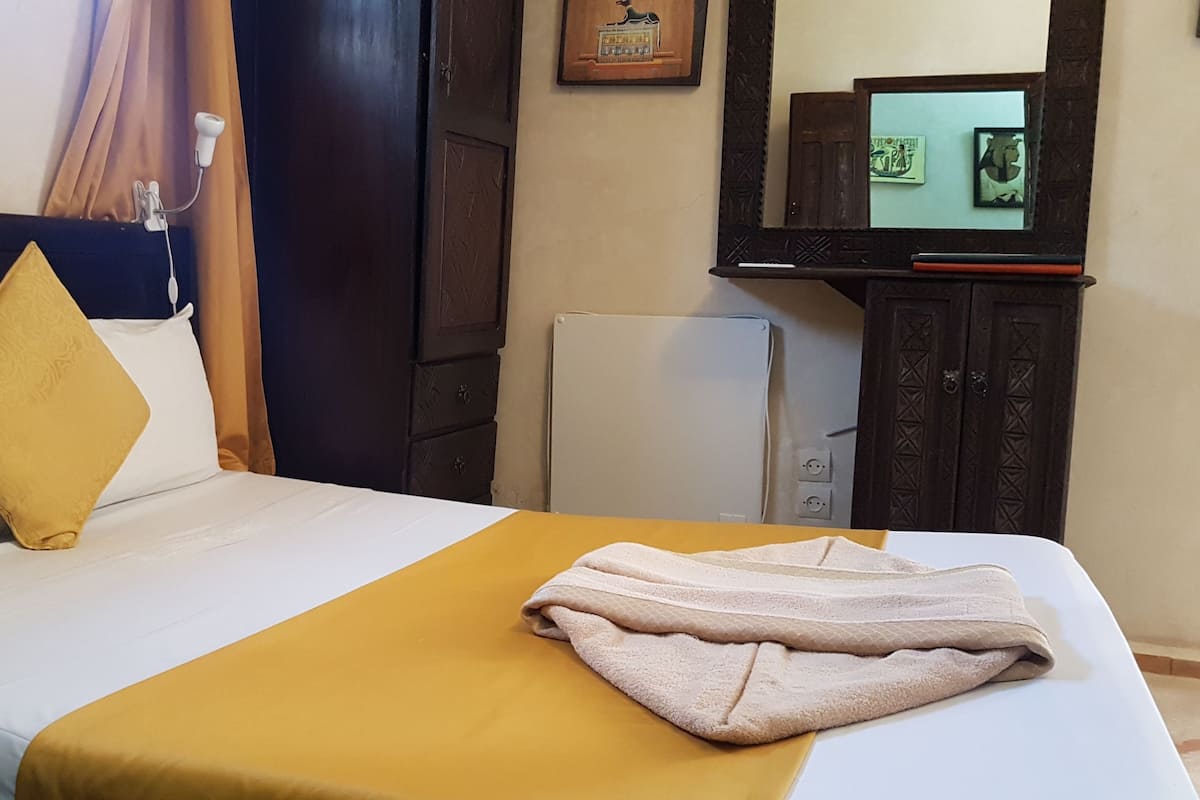 A hotel room with a bed, a TV on a stand, a small refrigerator, and a curtain.