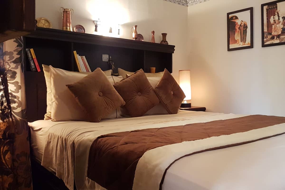 A neatly made bed with brown and white bedding, a bedside lamp, and a shelf with decorative items above it.