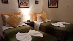 Habitación de hotel con dos camas, cada una con colcha verde a rayas y una toalla blanca. Hay dos lámparas en las mesitas de noche, y las paredes están decoradas con cuadros enmarcados.