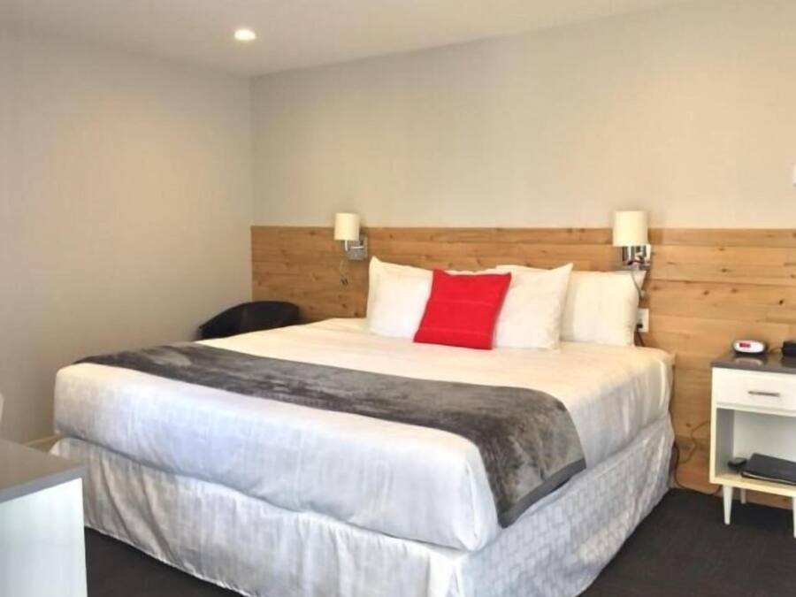 Hotelkamer met een groot bed, een houten hoofdbord, twee bedlampen en een klein bureau met stoel.