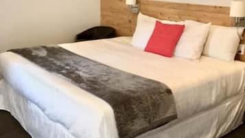 Un lit bien fait, avec une couette grise et blanche, un coussin rouge qui apporte une touche de couleur, et deux lampes fixées au mur.