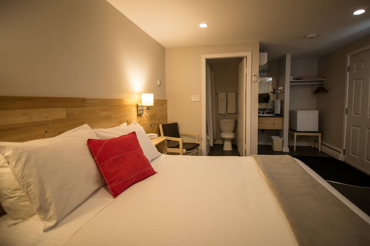 Una habitación de hotel con cama, escritorio, silla, baño y kitchenette.