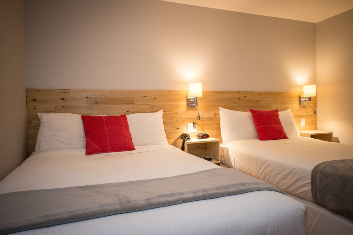Habitación de hotel con dos camas, cabeceros de madera, lámparas de noche y un teléfono en la mesita.