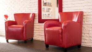 Deux fauteuils en cuir rouge dans une pièce dont un mur est en briques blanches et qui est agrémentée d’un miroir à cadre rouge.