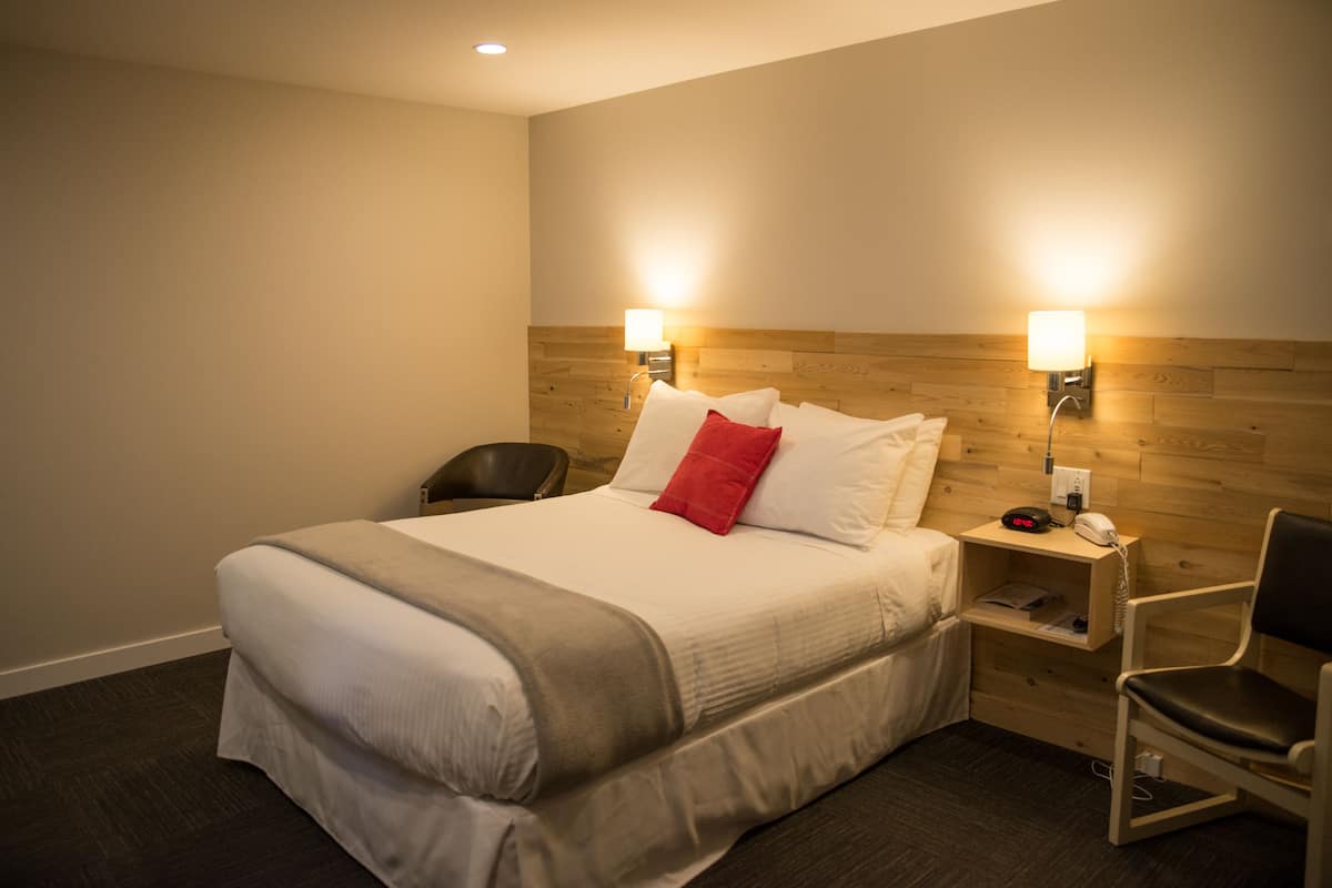 Una habitación de hotel con una cama grande, dos lámparas de noche, una silla y un cabecero de madera.