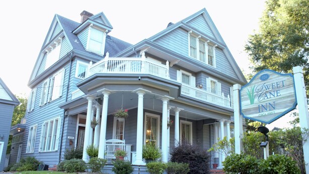 A large, two-story house with a porch and a sign for the Sweet Cane Inn.