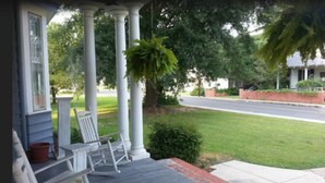 A porch with white columns, a wooden deck, and a view of a residential street.