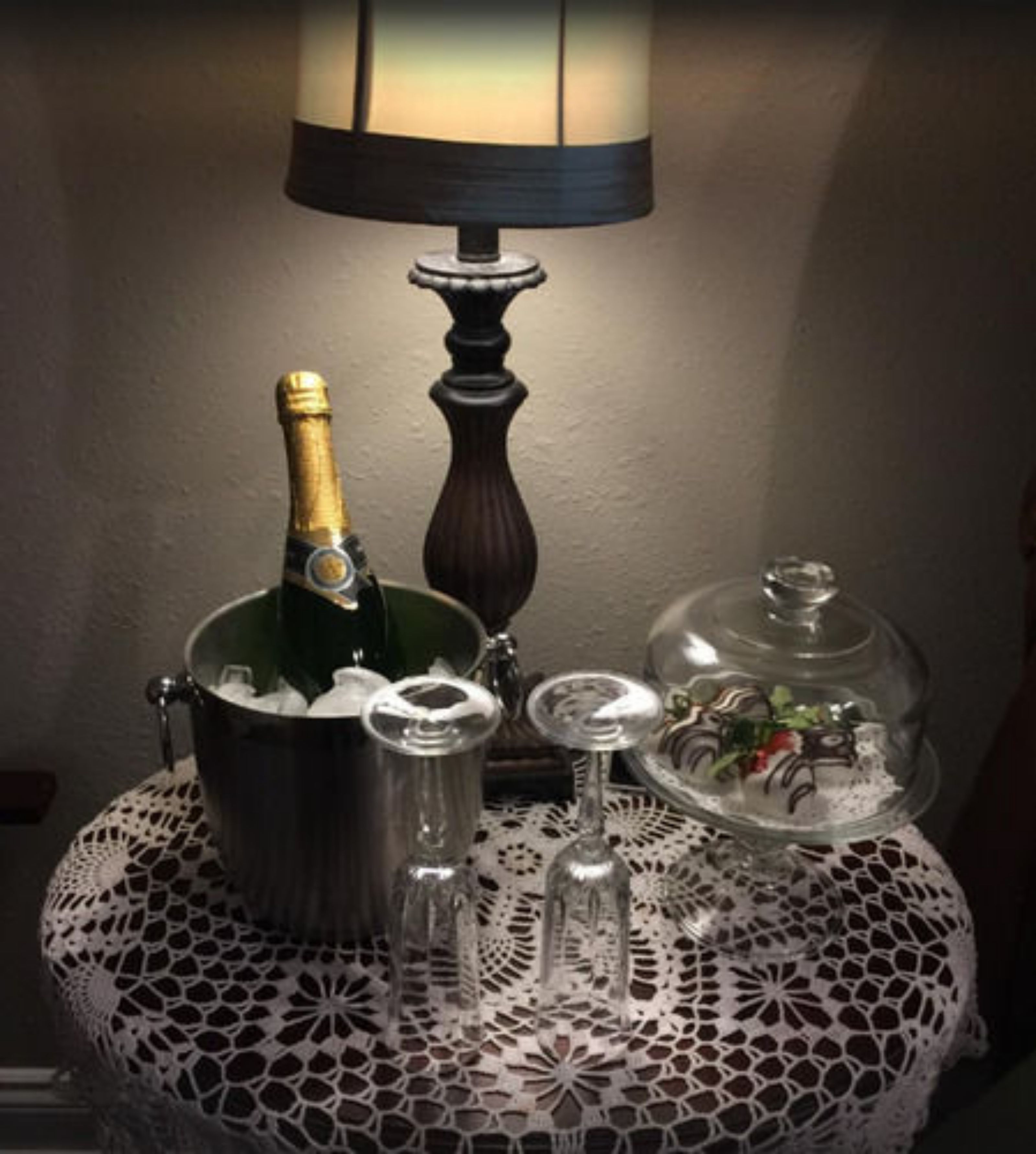 Una mesa con una botella de champán, una jarra de metal, un vaso y una cúpula de vidrio con comida.
