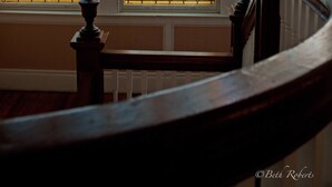 A staircase with a wooden handrail and a stained glass window with floral patterns.
