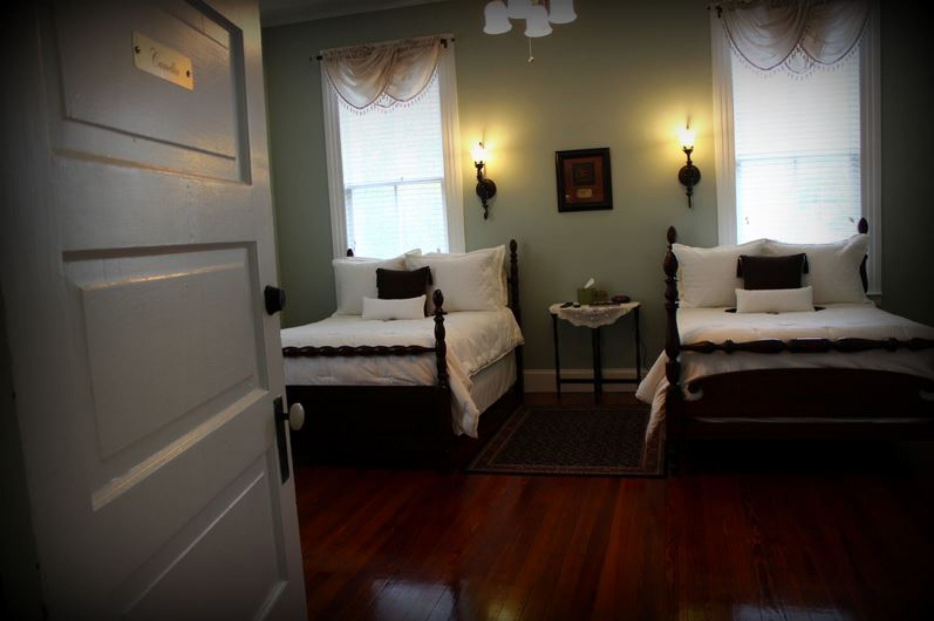 A room with two single beds, a small table, and two wall-mounted lamps.