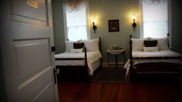 A room with two single beds, a small table, and two wall-mounted lamps.