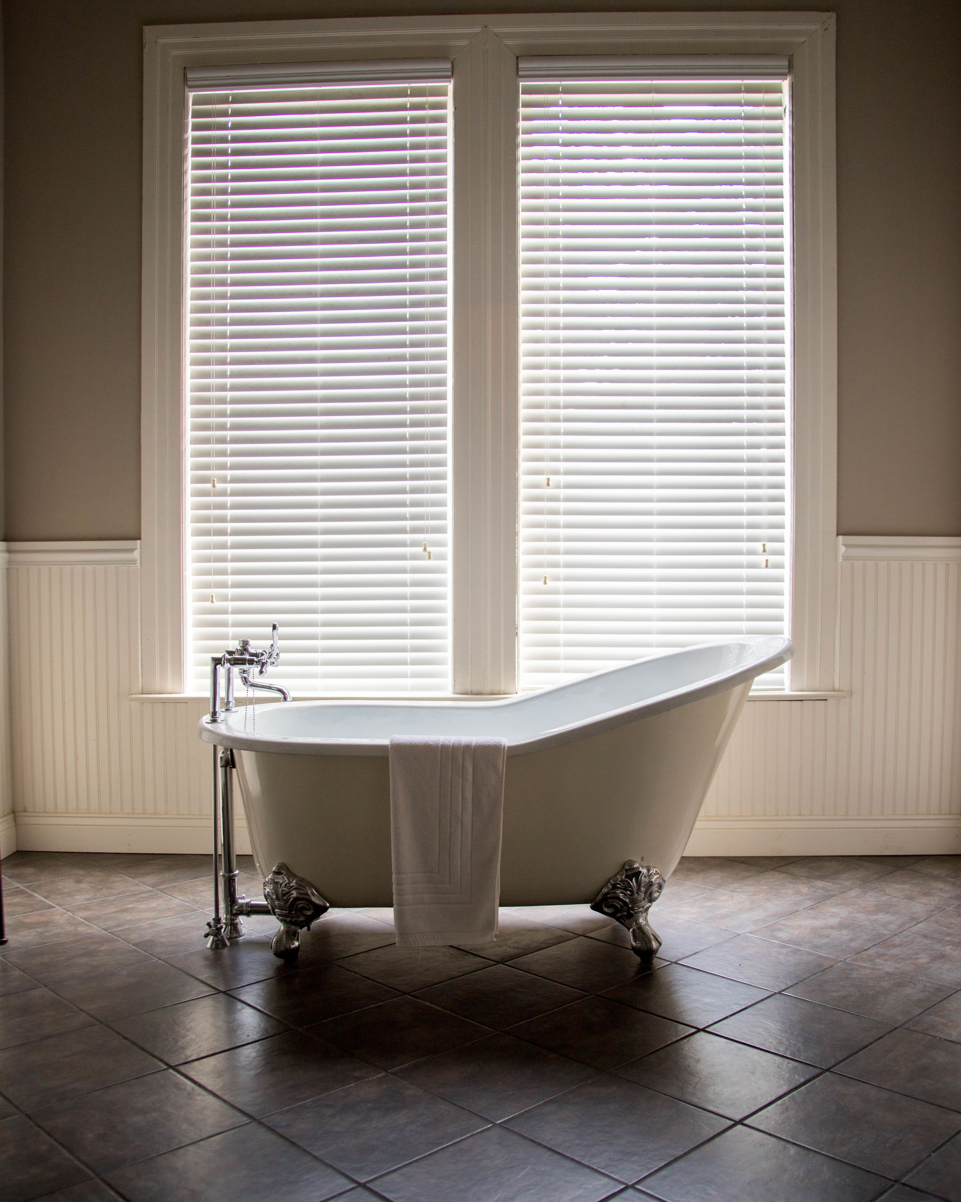 Een badkamer met een vrijstaand bad, witte wanden en een groot raam met zonwering.