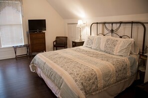 A bedroom with a bed, a television on a dresser, a chair, and a lamp.