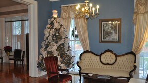 A room with a large Christmas tree, a vintage sofa, and a chandelier.