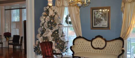 A room with a large Christmas tree, a vintage sofa, and a chandelier.