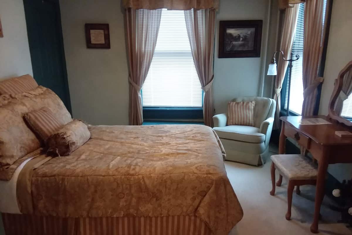A bedroom with a large bed, a chair, a desk, and a window with curtains.