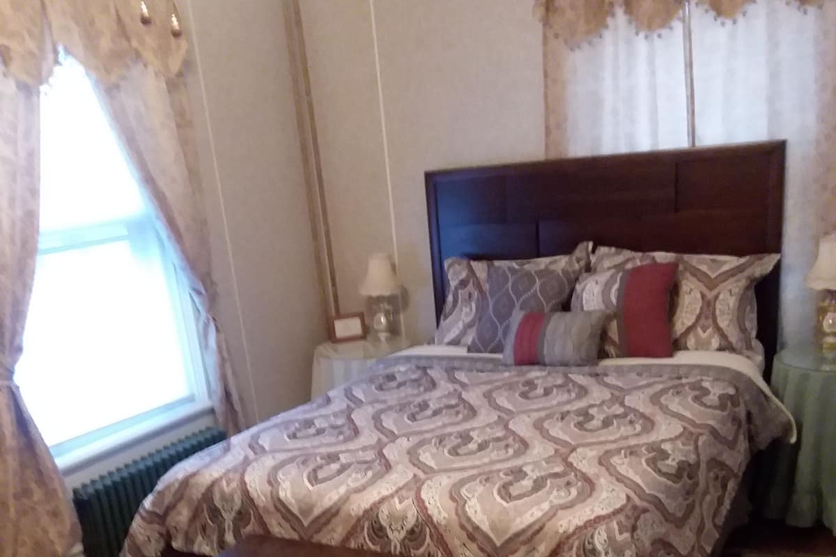 A bedroom with a large bed, a wooden nightstand, a bedside table, and a window with curtains.