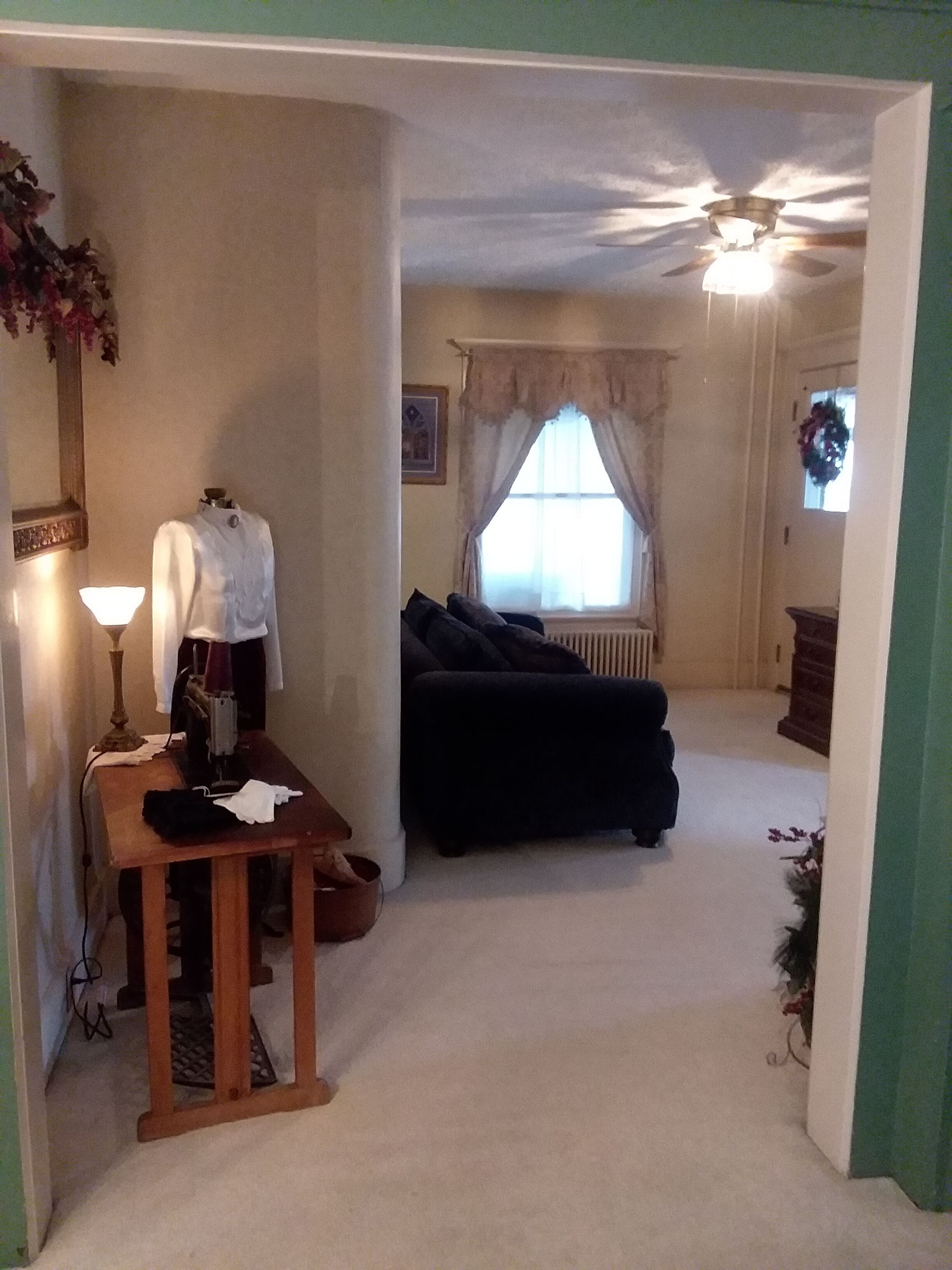 A compact living space with a sewing machine, a dining table, a black sofa, and a ceiling fan.