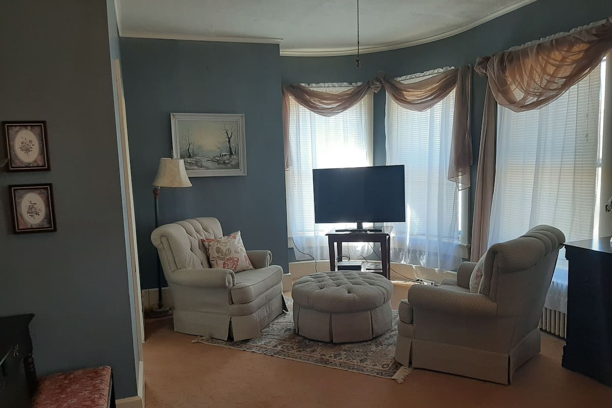 A living room with a television, two armchairs, a sofa, a small table, and a rug.