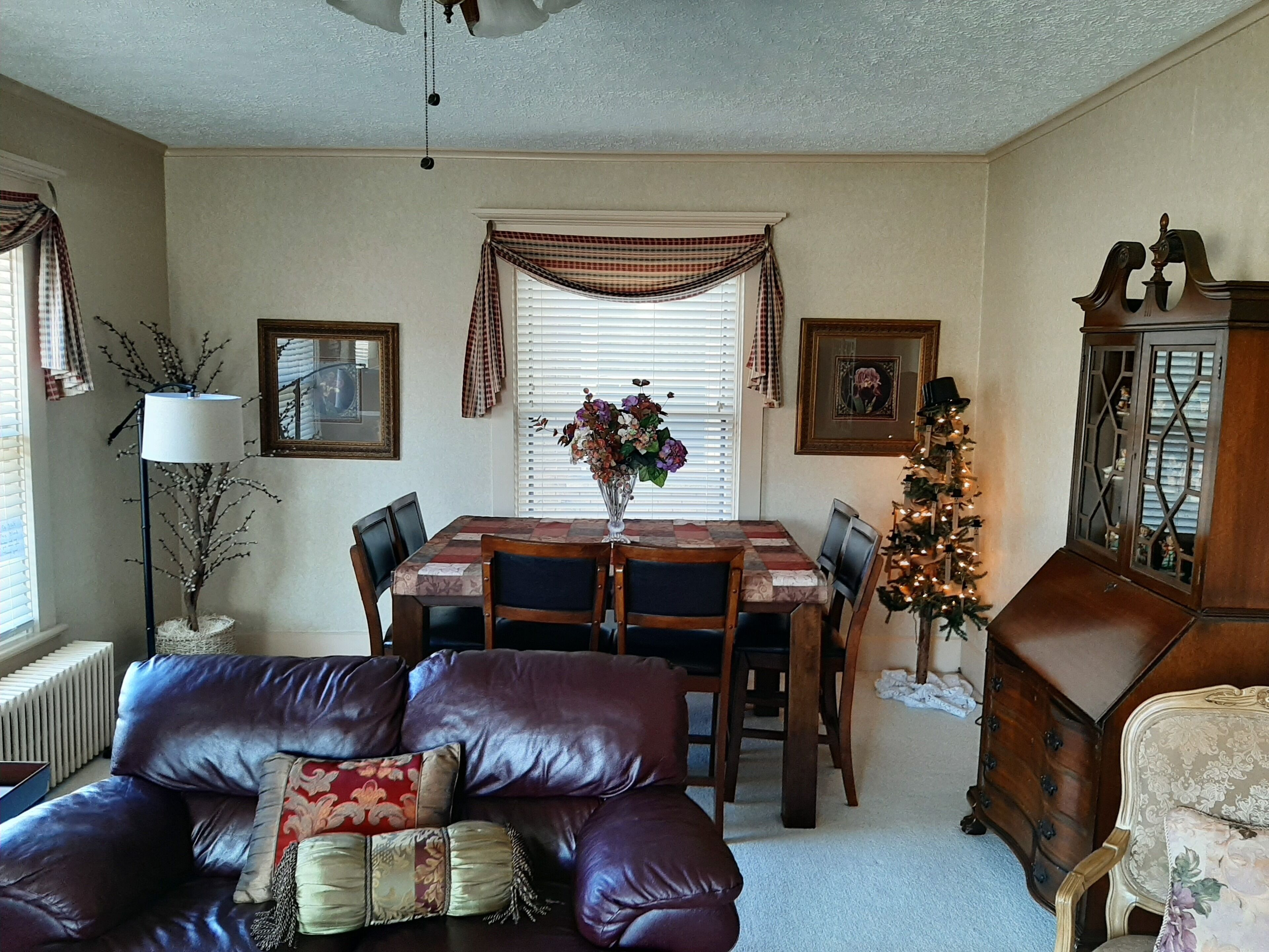 A dining area with a table, chairs, a vase of flowers, a Christmas tree, and a sofa with cushions.