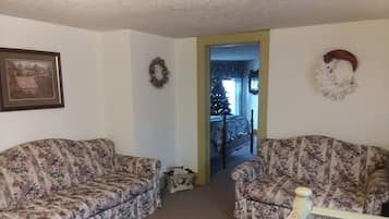 A living room with two floral-patterned sofas, a framed picture on the wall, a wreath, and a Christmas tree in the background.