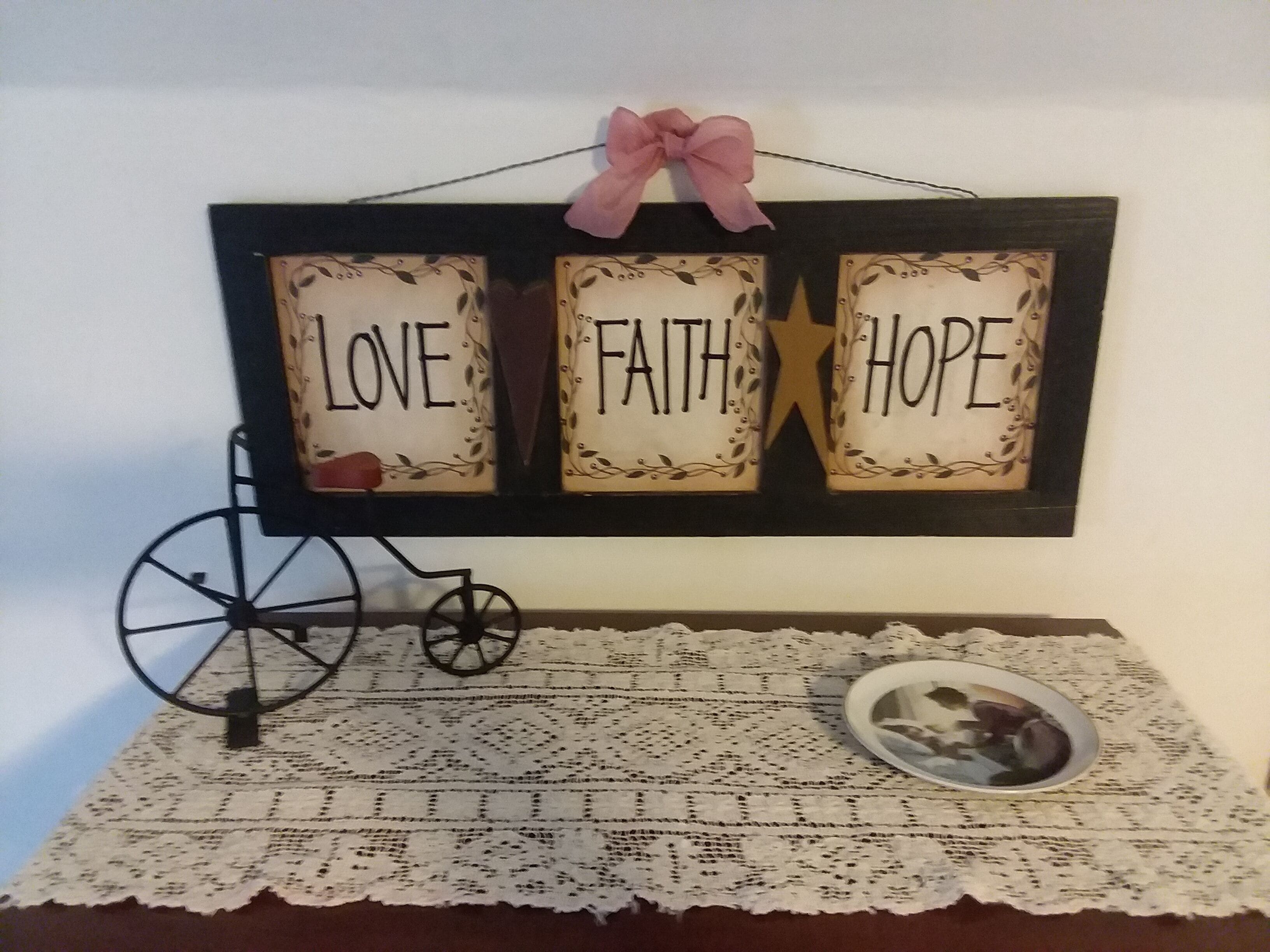 Un letrero en la pared con las palabras AMOR, FE, ESPERANZA y un lazo rosa.