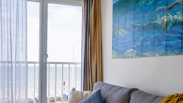 A living room with a grey sofa, a yellow throw blanket, and a painting of sailboats on the wall. - Boulevard 5 (Zandvoort)