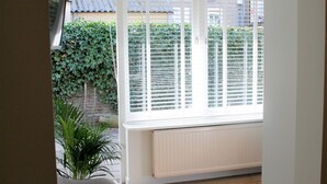 A room with a large window, a radiator, a grey sofa, and a hanging light fixture. - Boulevard 5 (Zandvoort)